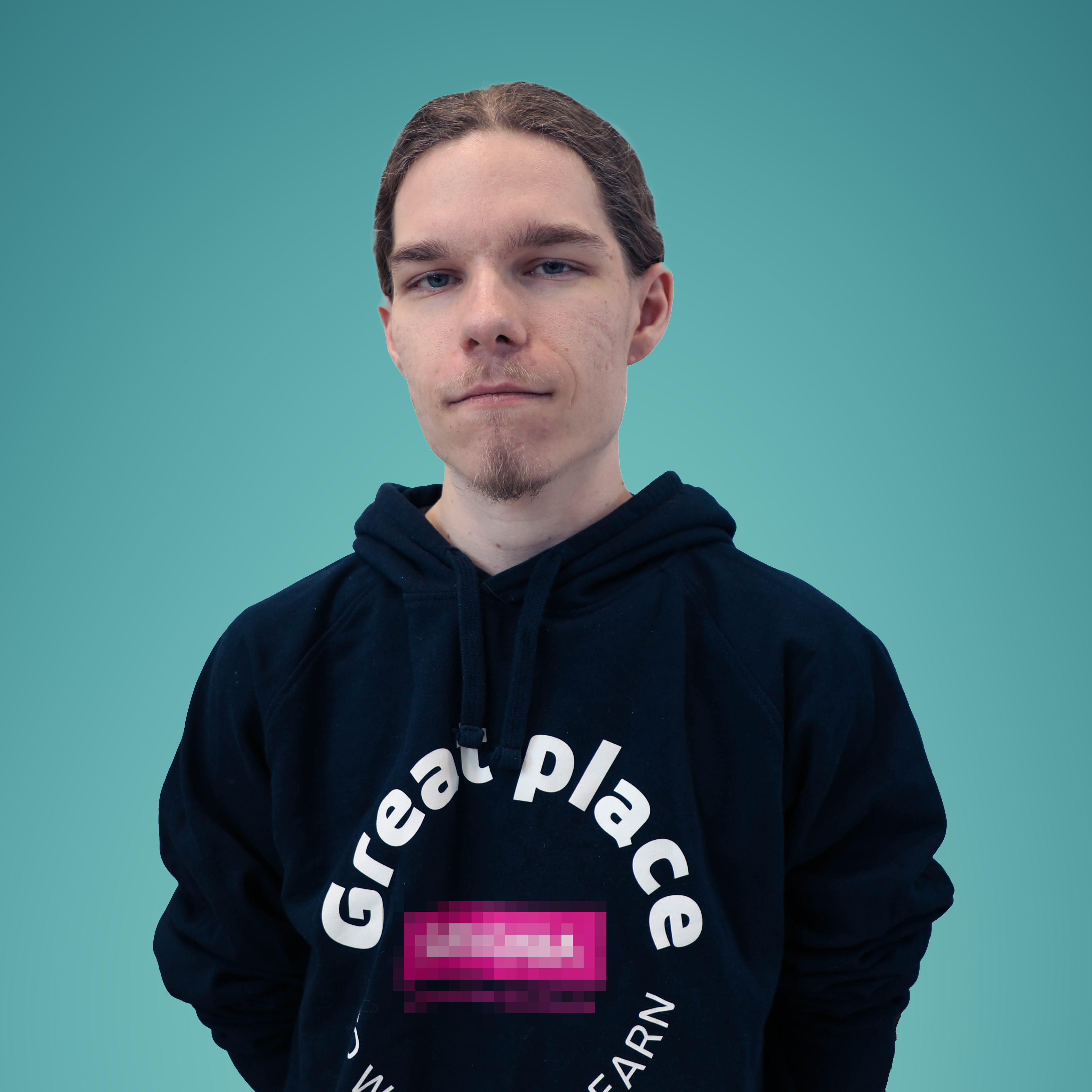 Vaaleaihoinen nuori henkilö, jolla on pitkät taakse sidotut hiukset ja jolla on tumma huppari, jossa on osittain epäselvä teksti, seisoo neutraalilla ilmeellä kameraan päin vaaleanruskeaa taustaa vasten.